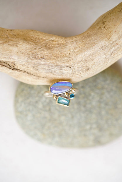 Ring with opal and blue gemstones on a piece of driftwood