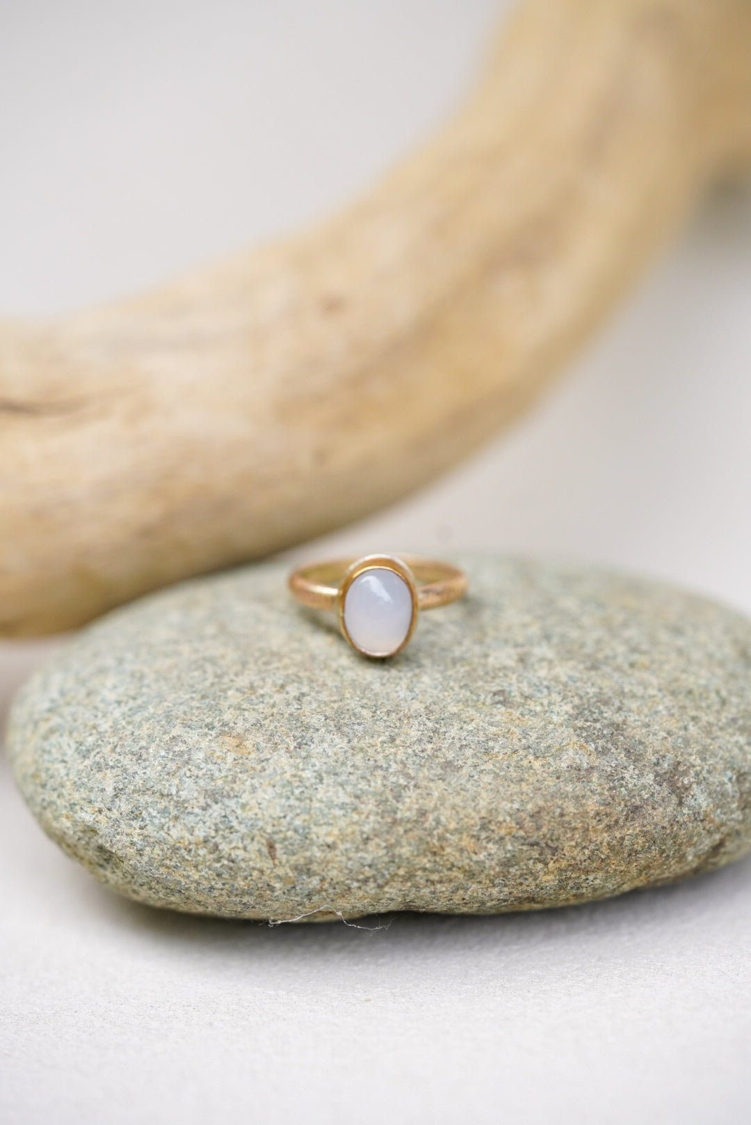 Light purple chalcedony stone with gold ring on a rock next to driftwood