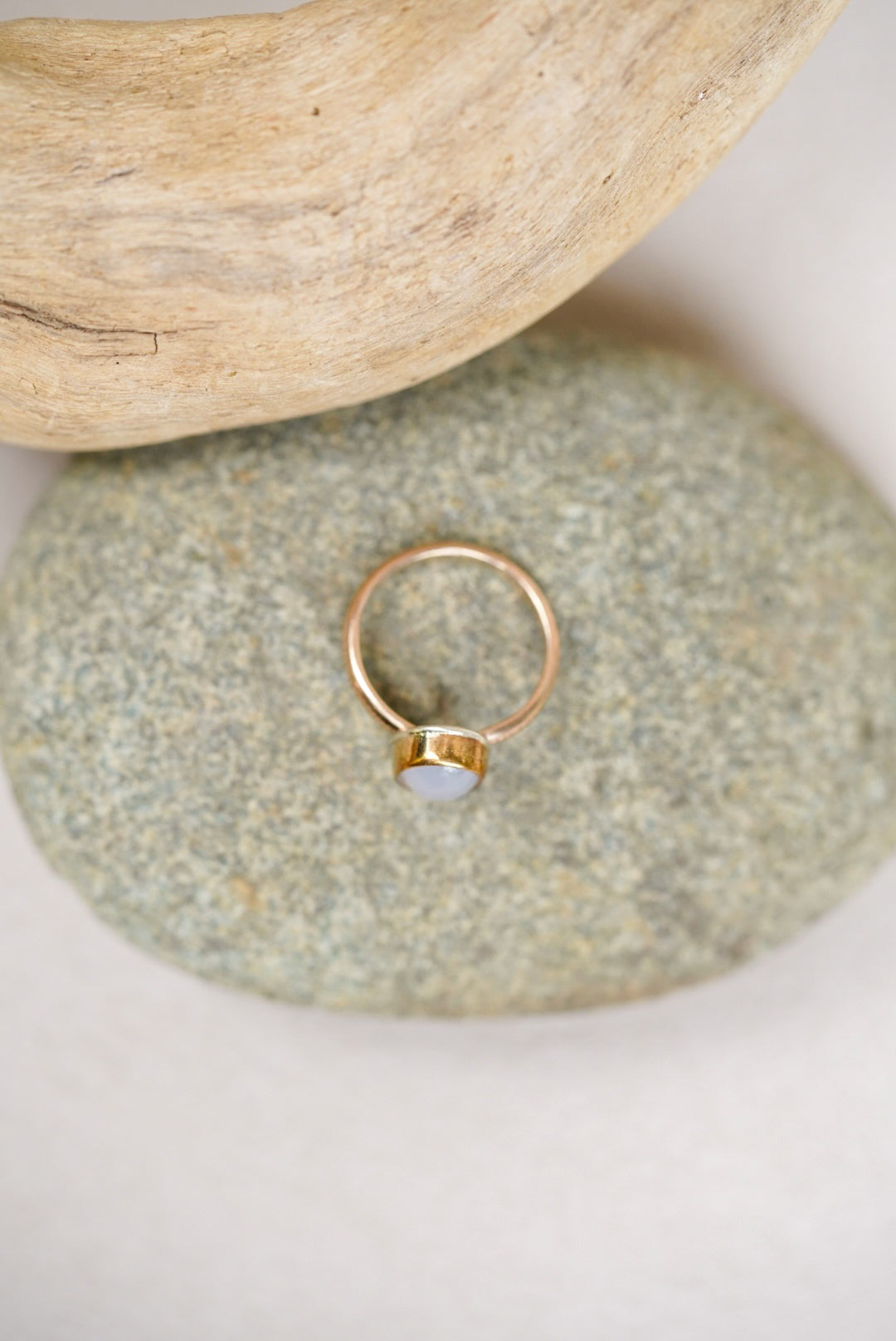 Light purple chalcedony stone with gold ring on a rock next to driftwood
