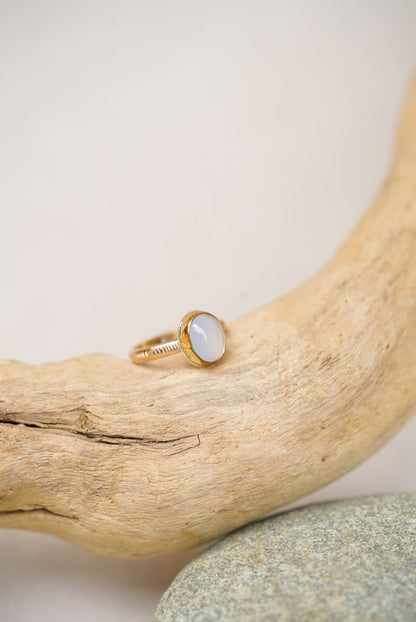Light purple chalcedony stone with gold ring on a rock next to driftwood