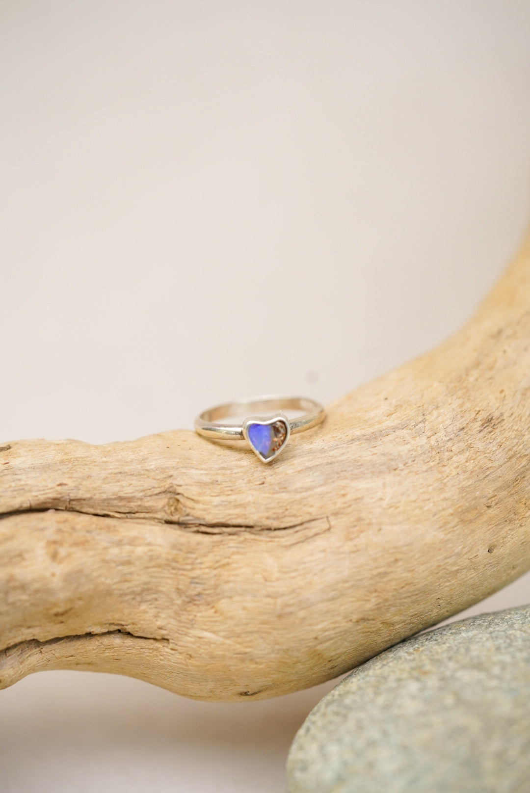 Silver ring with a purple/blue heart-shaped stone on a piece of driftwood.