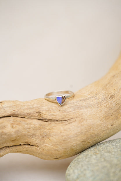 Silver ring with a purple/blue heart-shaped stone on a piece of driftwood.