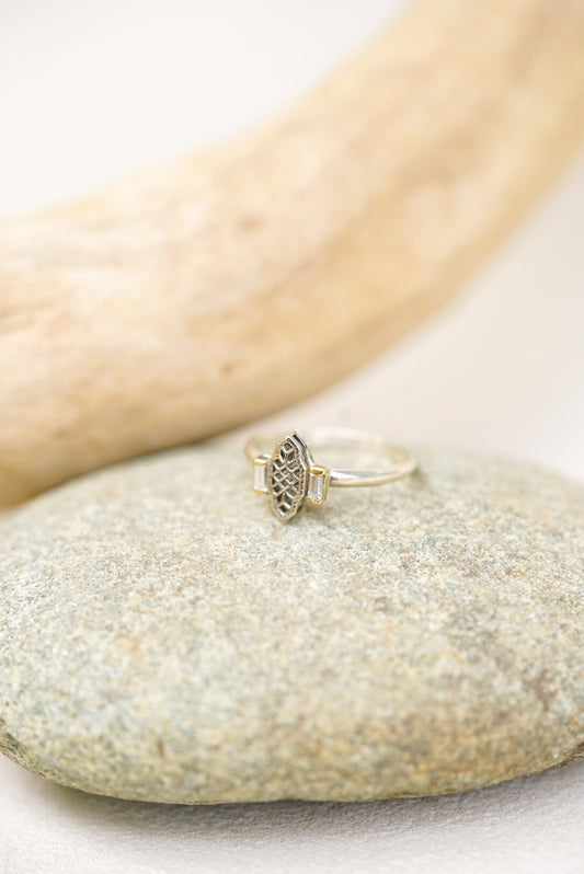 Silver ring with intricate design and diamonds on a stone surface