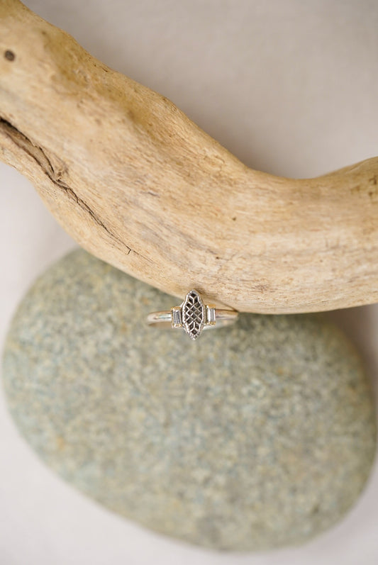 Silver ring with intricate design and diamonds on a piece of driftwood and stone
