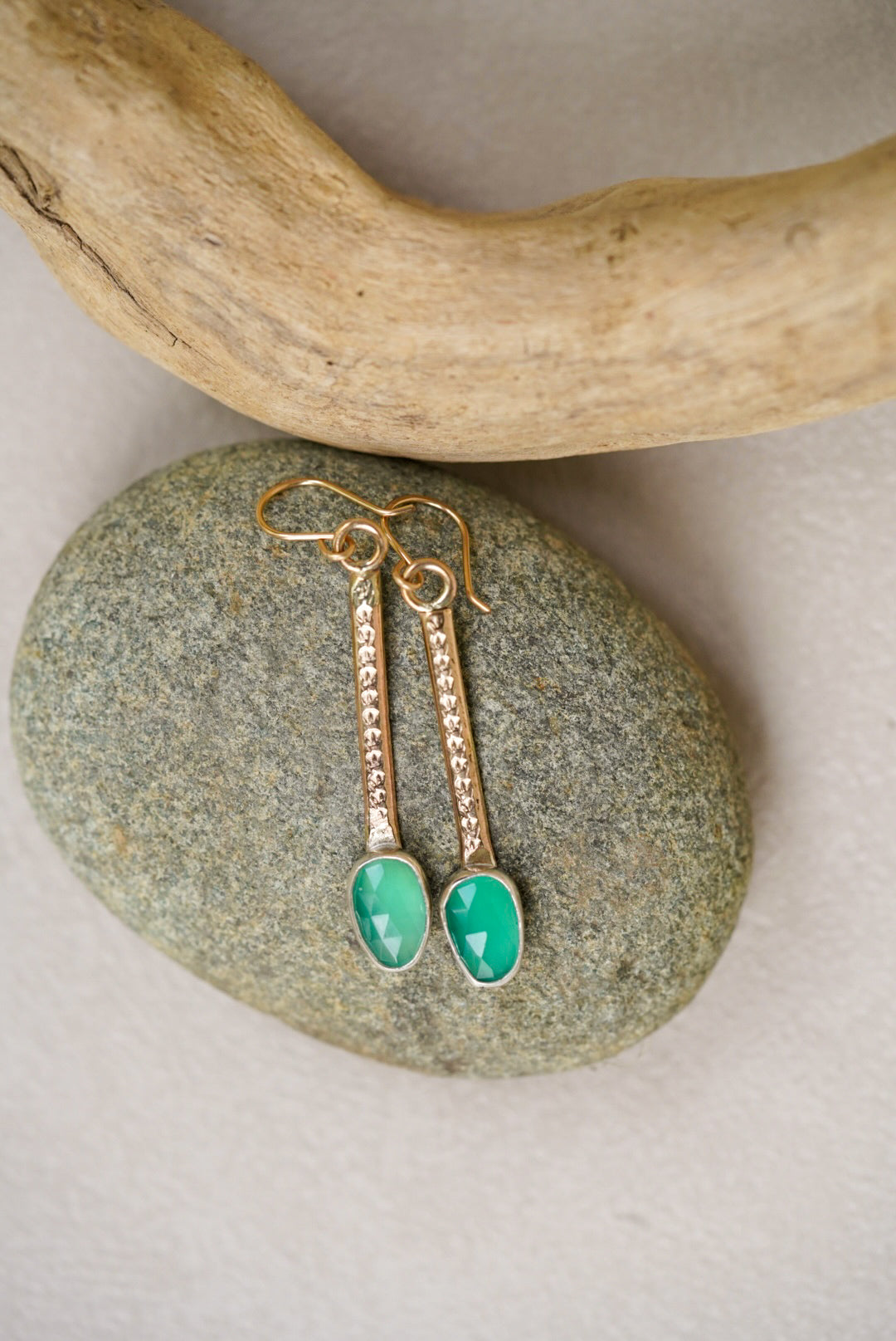 Gold earrings with green gemstones on a stone surface