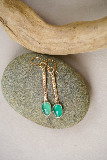 Gold earrings with green gemstones on a stone surface