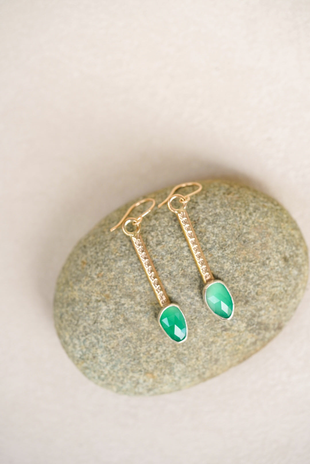 Gold earrings with green gemstones on a stone surface
