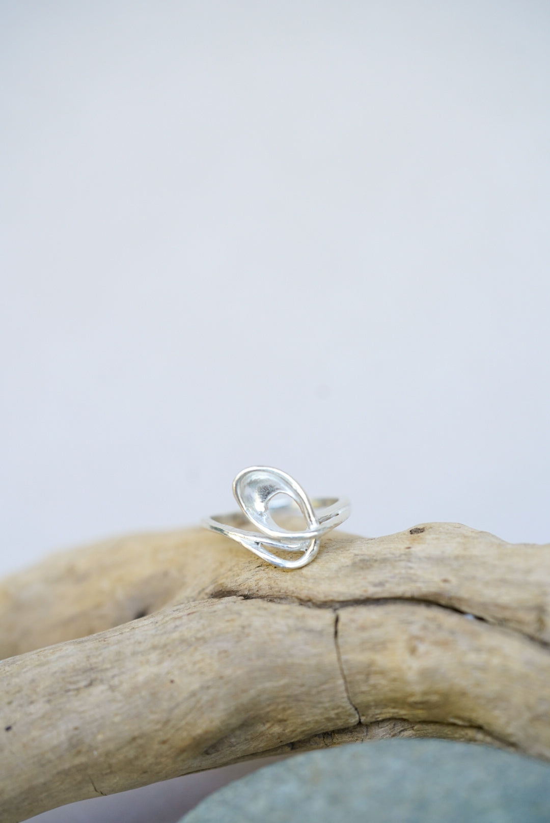 Silver ring on a piece of driftwood with a light gray background