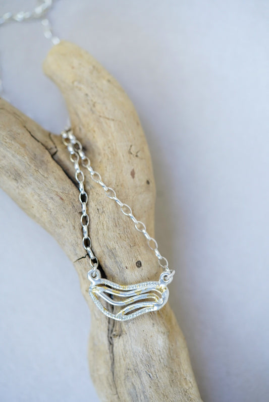 Silver necklace with a wave design pendant on a piece of driftwood.