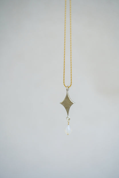 Necklace with a diamond-shaped pendant and gold chain on a light gray background