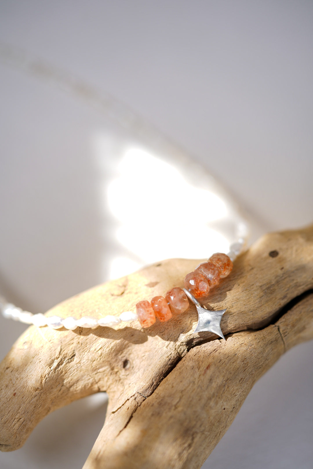 Necklace with sunstone and pearl beads on a piece of driftwood against a white background