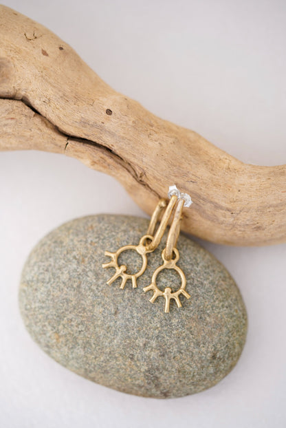 Gold earrings with sun designs on a stone and driftwood background