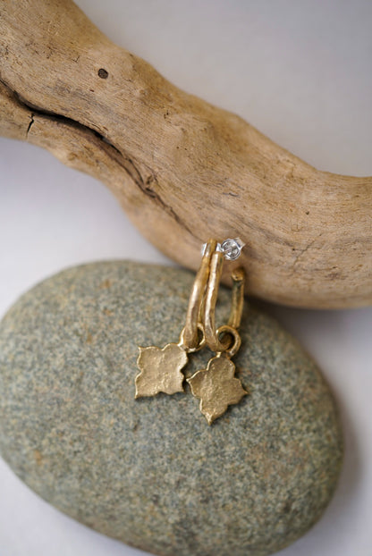 Gold earrings with charms on a stone surface