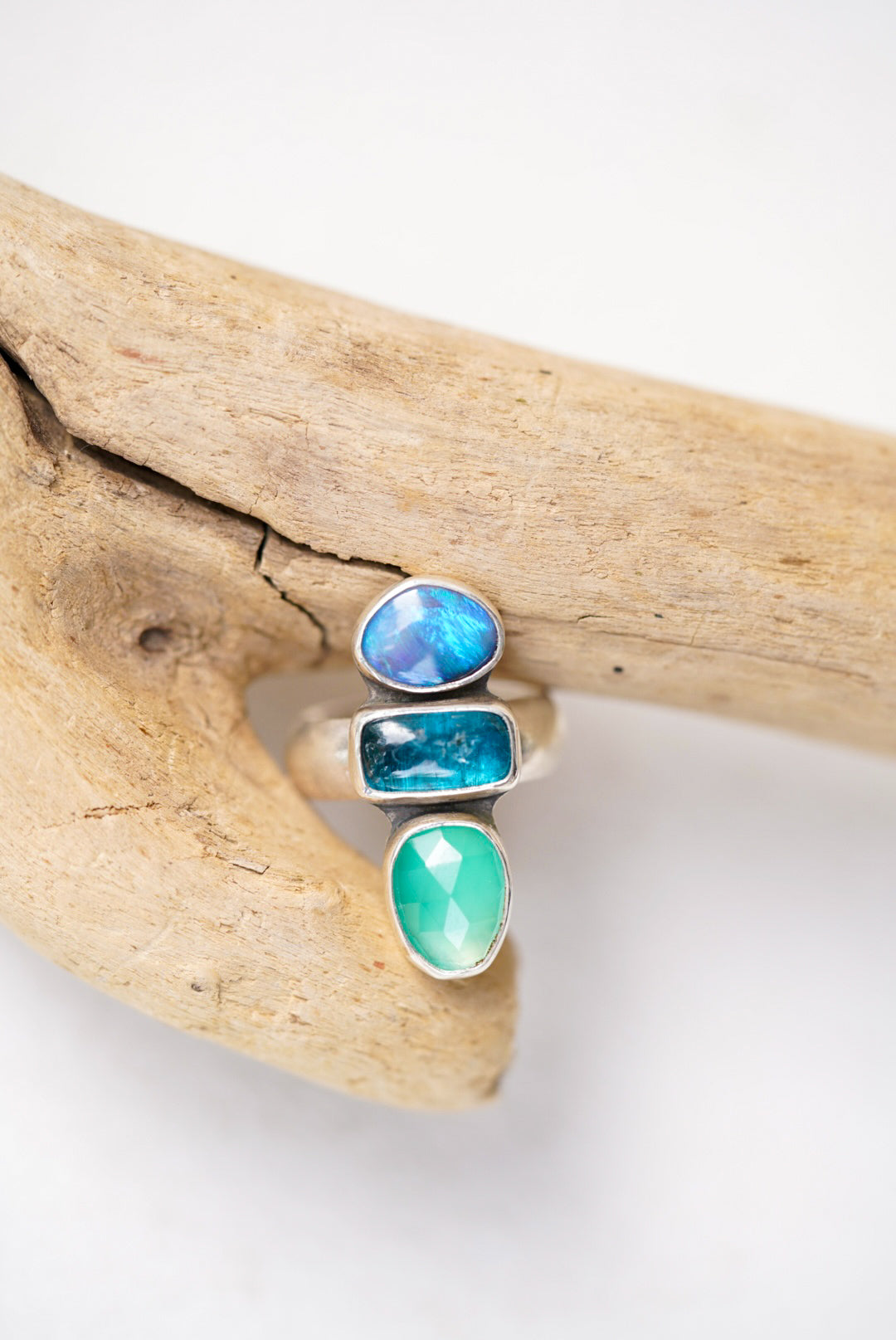 Ring with blue and green stones on a piece of driftwood