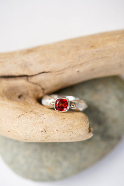 Bright red sunstone silver ring next to a piece of driftwood