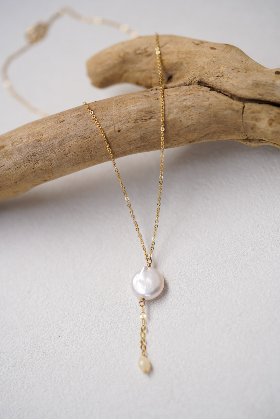 Gold necklace with a pearl pendant on a light gray background