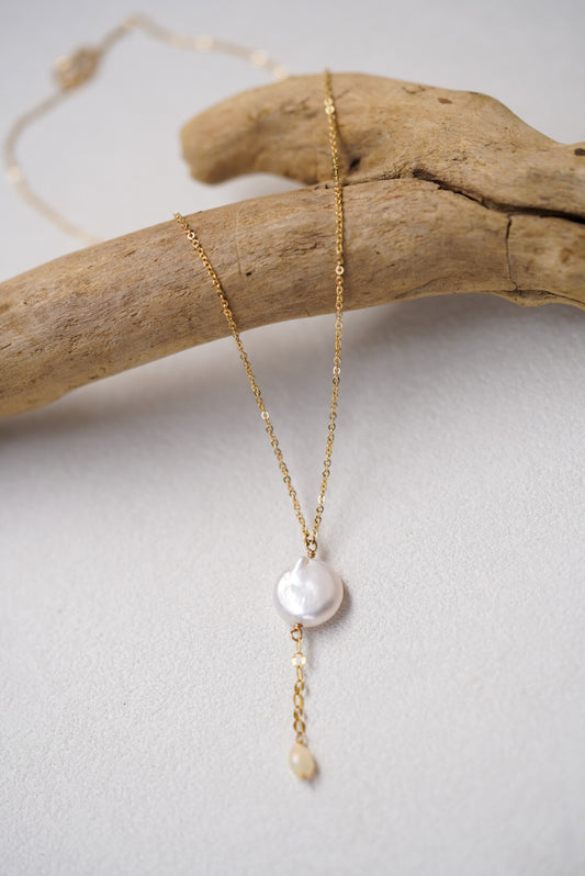 Gold necklace with a pearl pendant on a light gray background