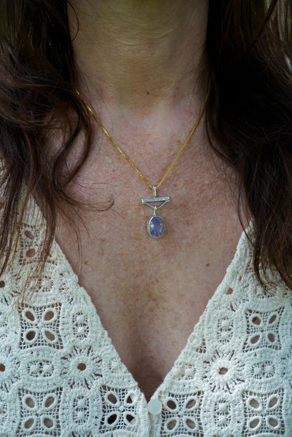 Close-up of a person wearing a gold necklace with a pendant, focusing on the neck and shoulders.