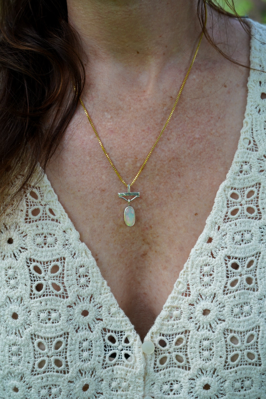 Necklace with a pendant worn by a person in a light-colored lace garment.