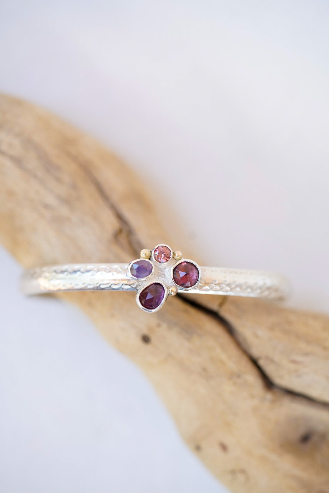 Silver cuff with gemstones on a piece of driftwood