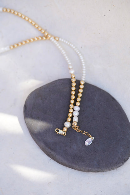 A delicate beaded necklace with pearl beads and gold spacer beads, displayed on a dark gray stone against a light beige background, showing the lobster clasp.