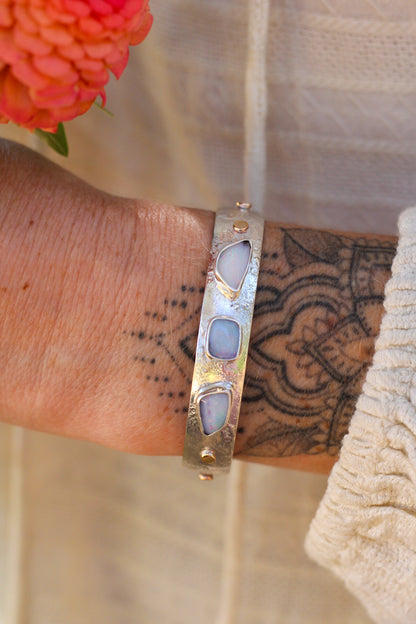 Silver bracelet with three Australian opal stones on a wrist with tattoos, next to a orange flower.