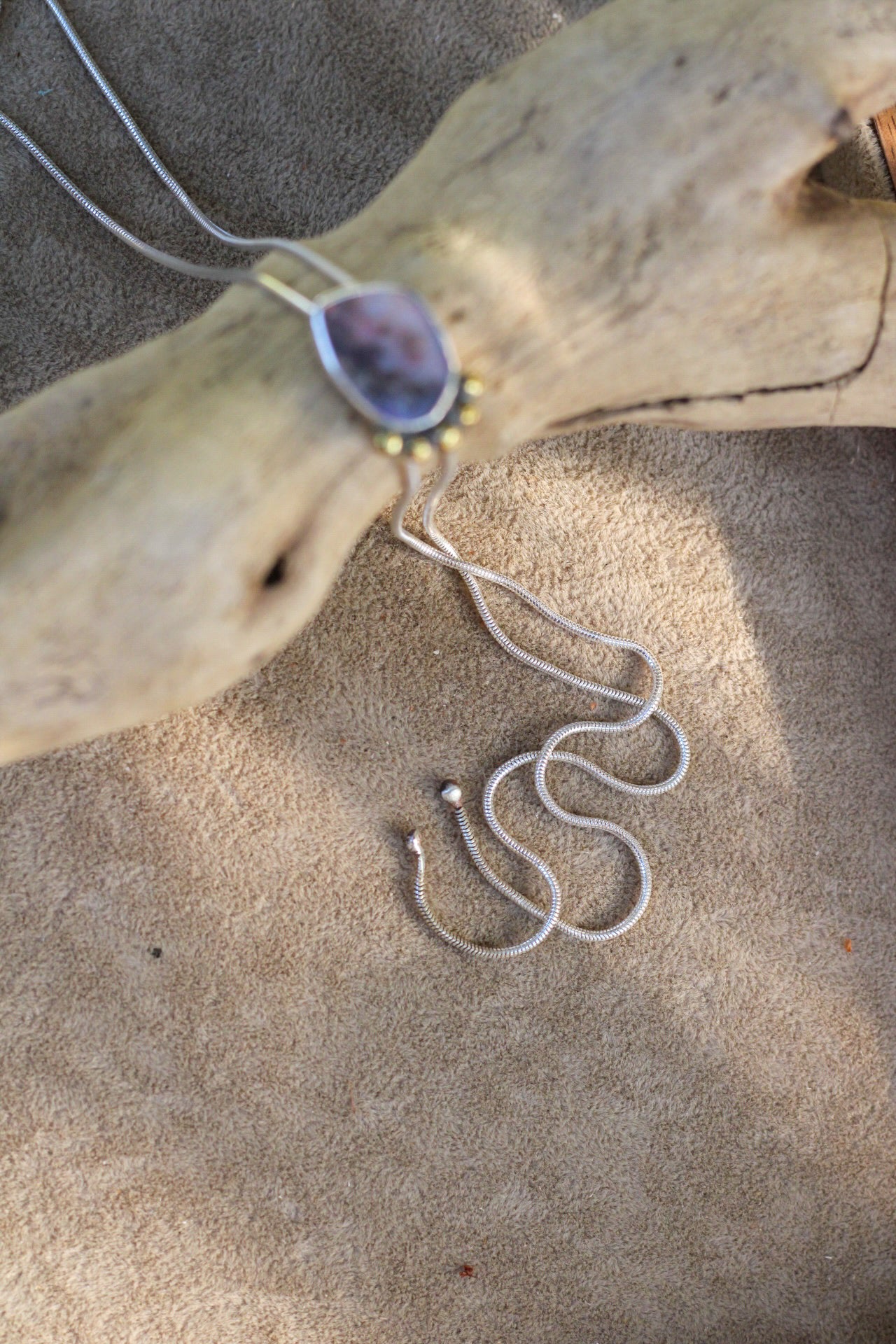 Necklace with a pendant on a piece of driftwood on sand