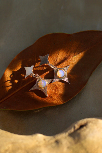 Star-shaped earrings with opals on a brown leaf