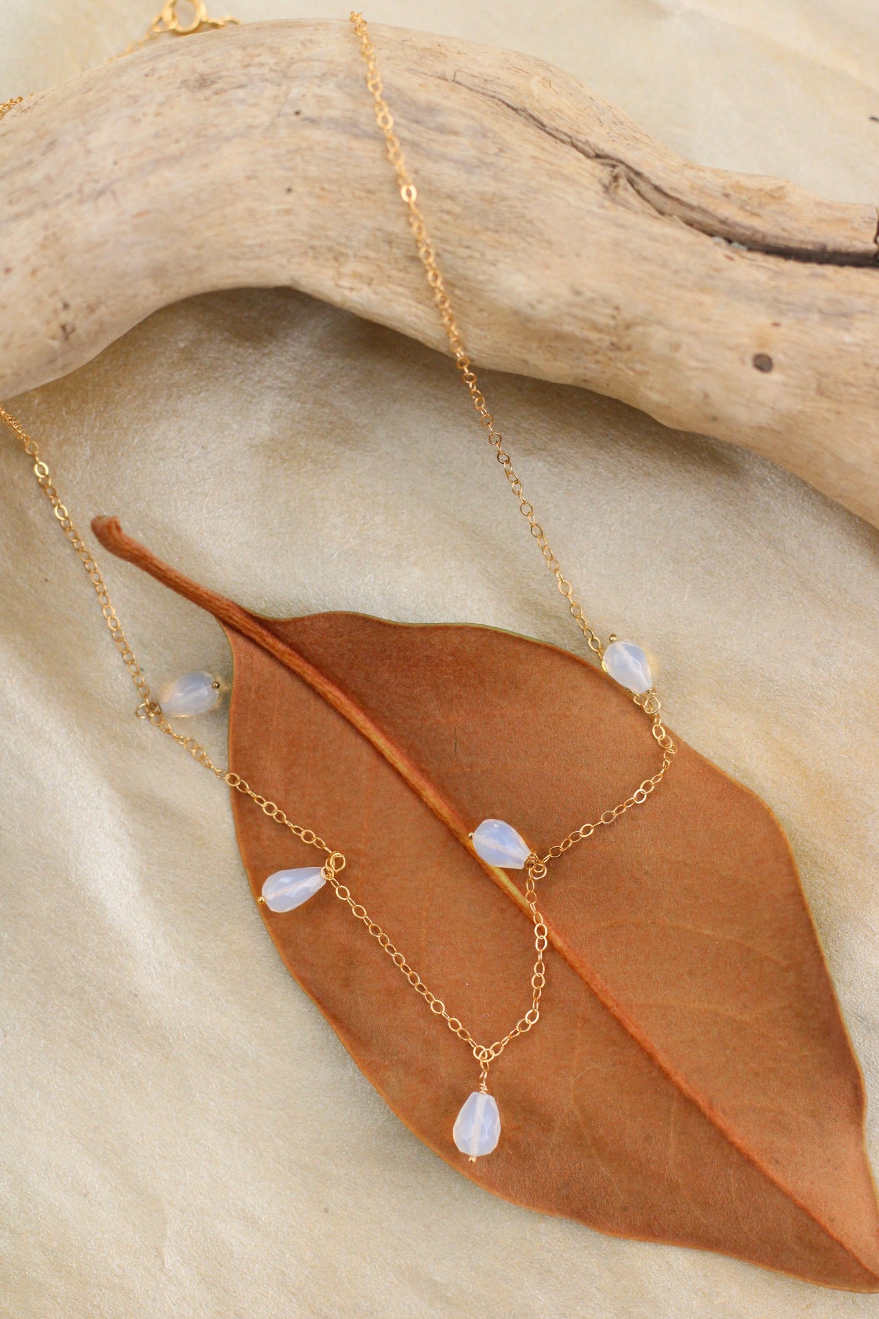 Gold necklace with opal beads on a leaf and wooden surface