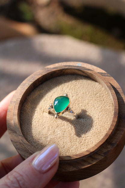 bright green stone in a gold ring in a wooden box on a stone background