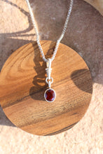Load image into Gallery viewer, Silver necklace with a red gemstone pendant on a wooden surface
