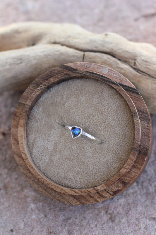 Heart-shaped blue opal gemstone ring on a wooden ring box with a natural background