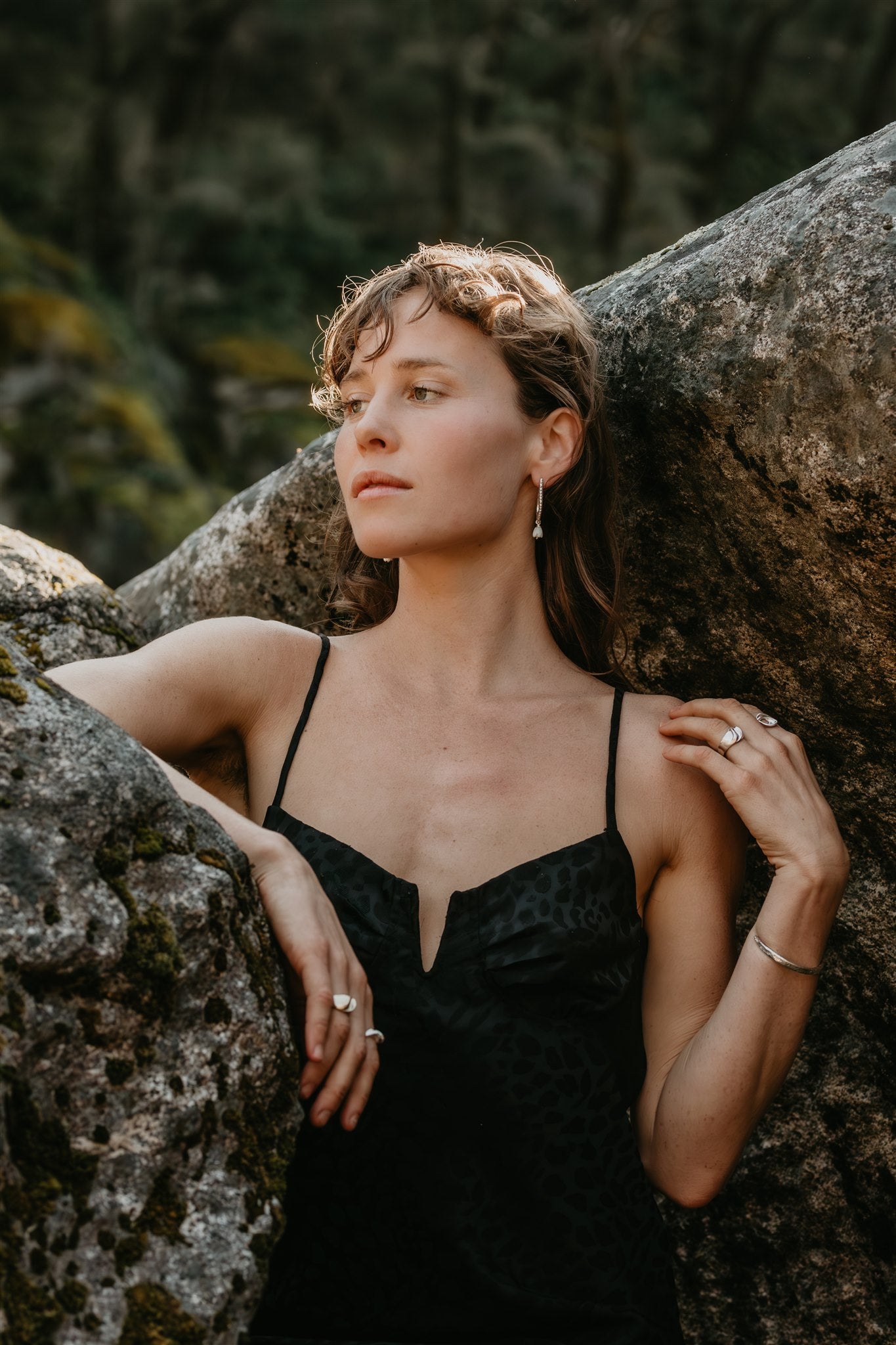 Woman in a black dress leaning against a large rock with a natural background