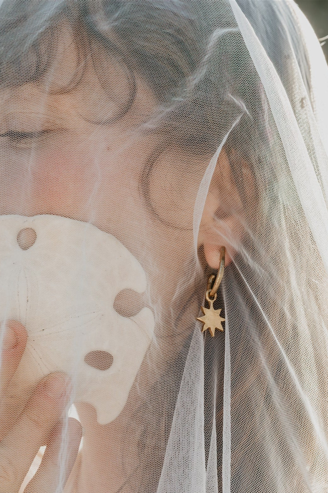 Person wearing a gold earring with a star design, holding a shell, and wearing a veil.
