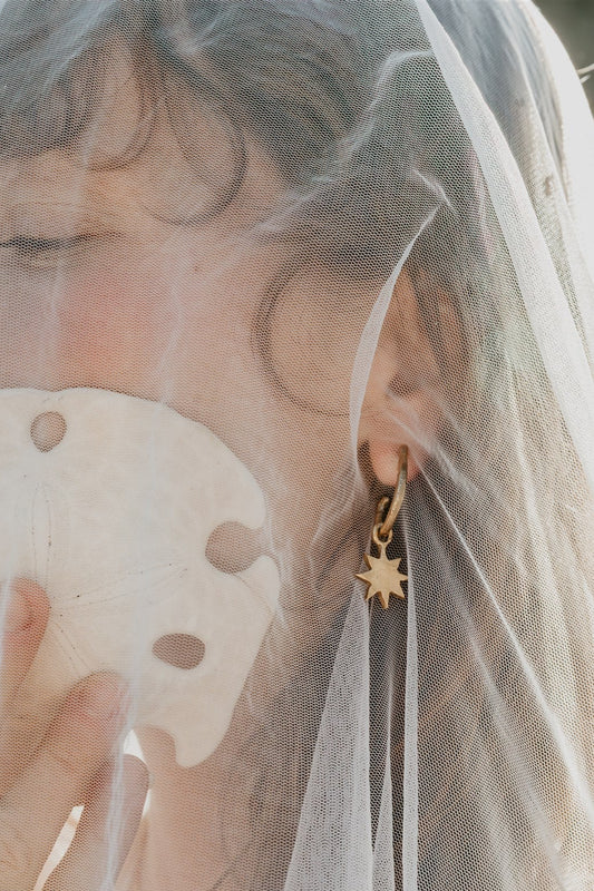 Person wearing a gold earring with a star design, holding a shell, and wearing a veil.