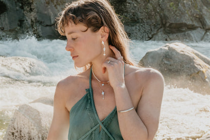Woman wearing earrings and a necklace by a rocky water source