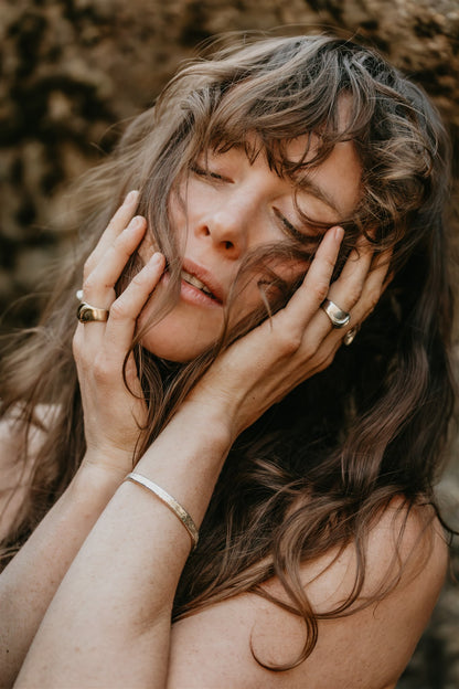 Woman with long hair and rings on her fingers against a blurred natural background