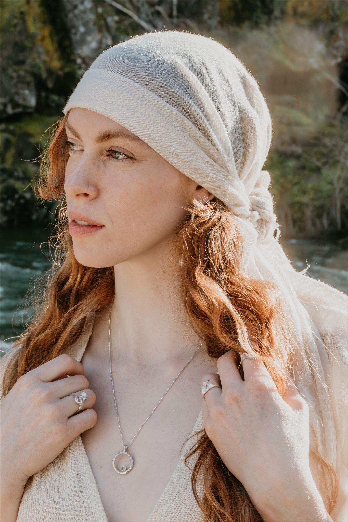 Woman with a headscarf and braided hair standing outdoors near water
