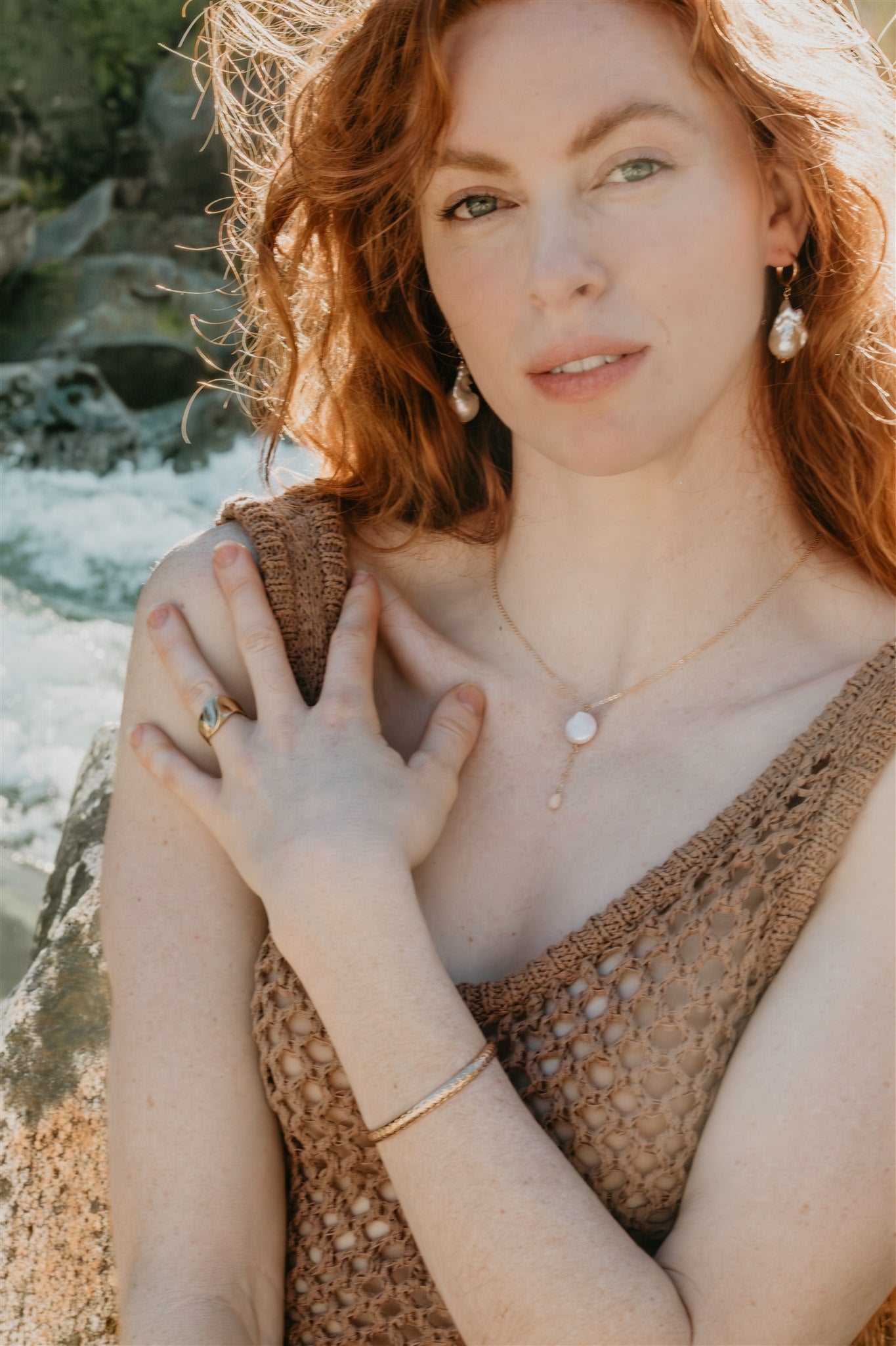 Woman wearing a brown top and jewelry by a natural setting