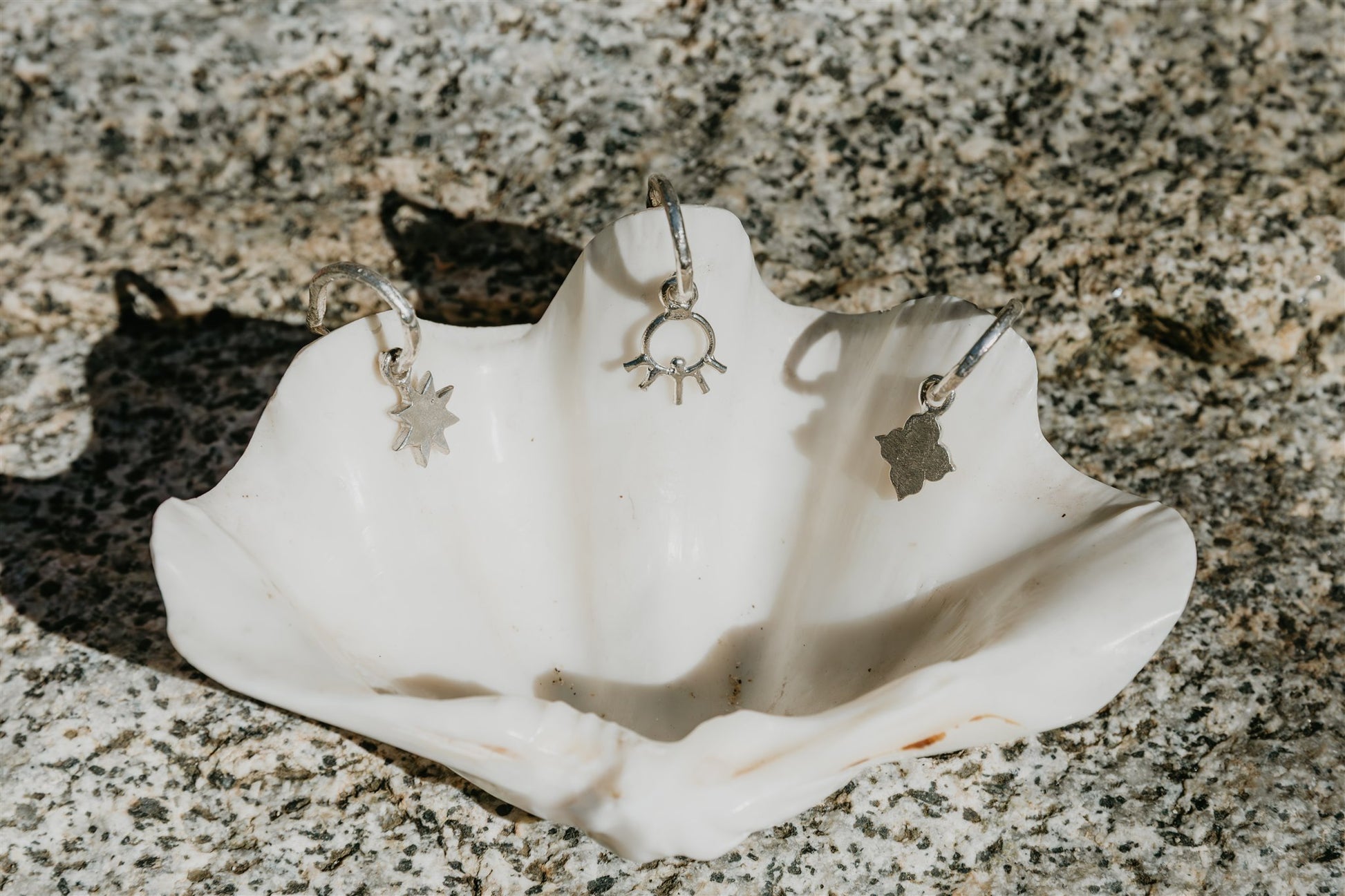 Silver earrings displayed on a white shell against a textured stone background