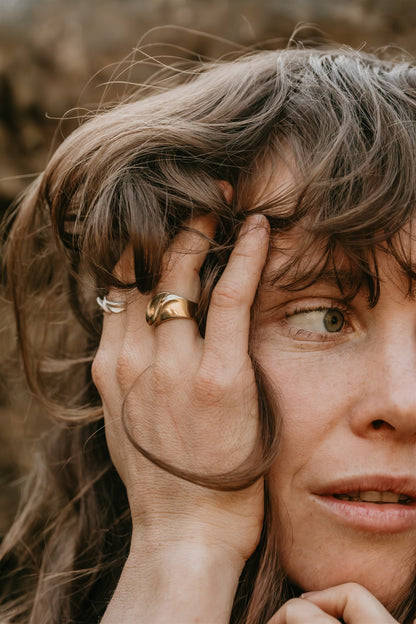 Close-up of a person with a hand on their head, wearing a gold ring.