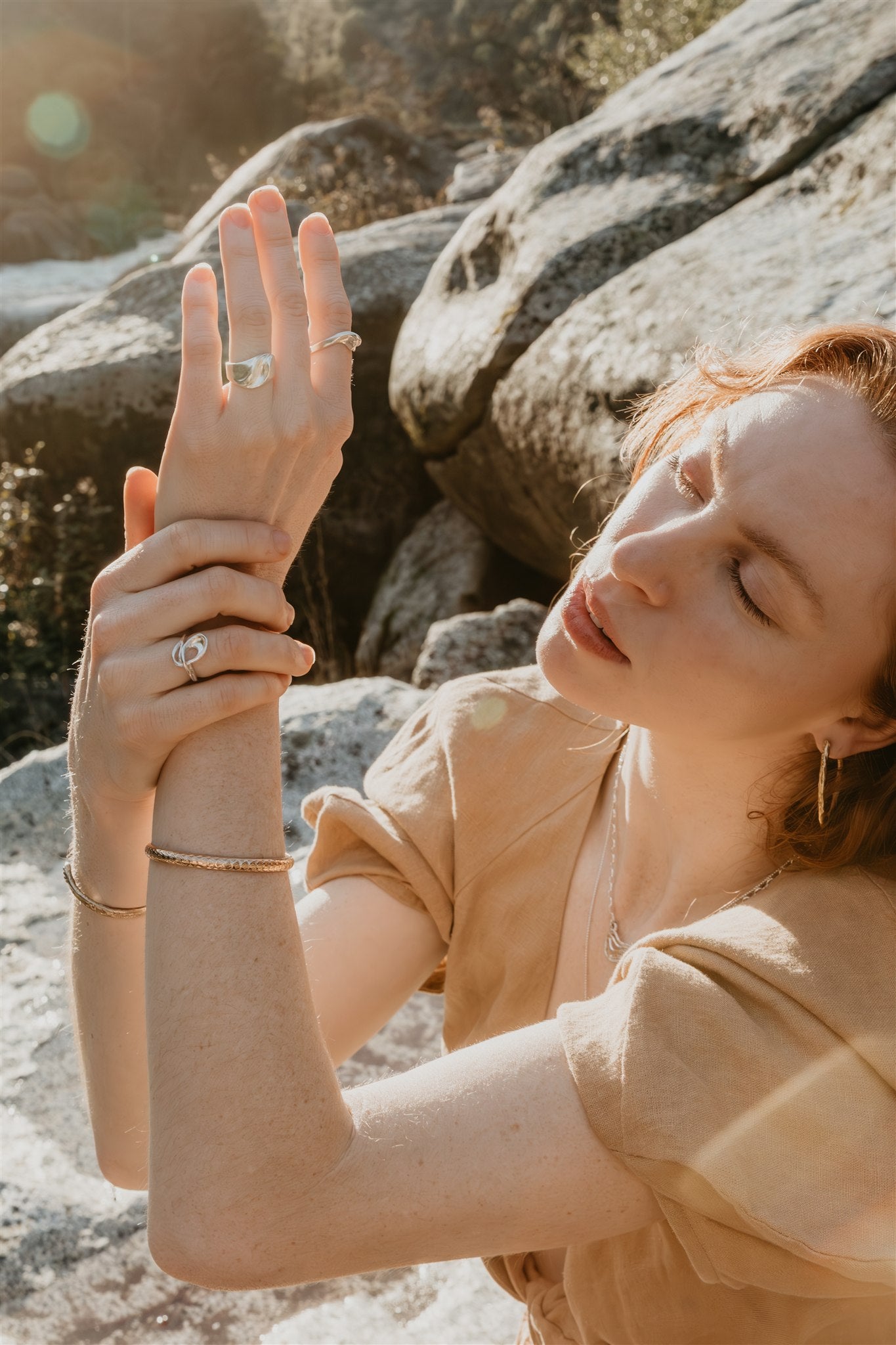 Woman in a beige dress holding her hand with rings outdoors near rocks