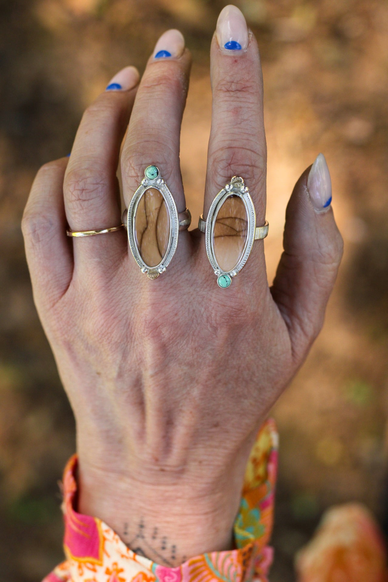 Hand wearing two silver rings with jasper and variscite stones against a blurred natural background