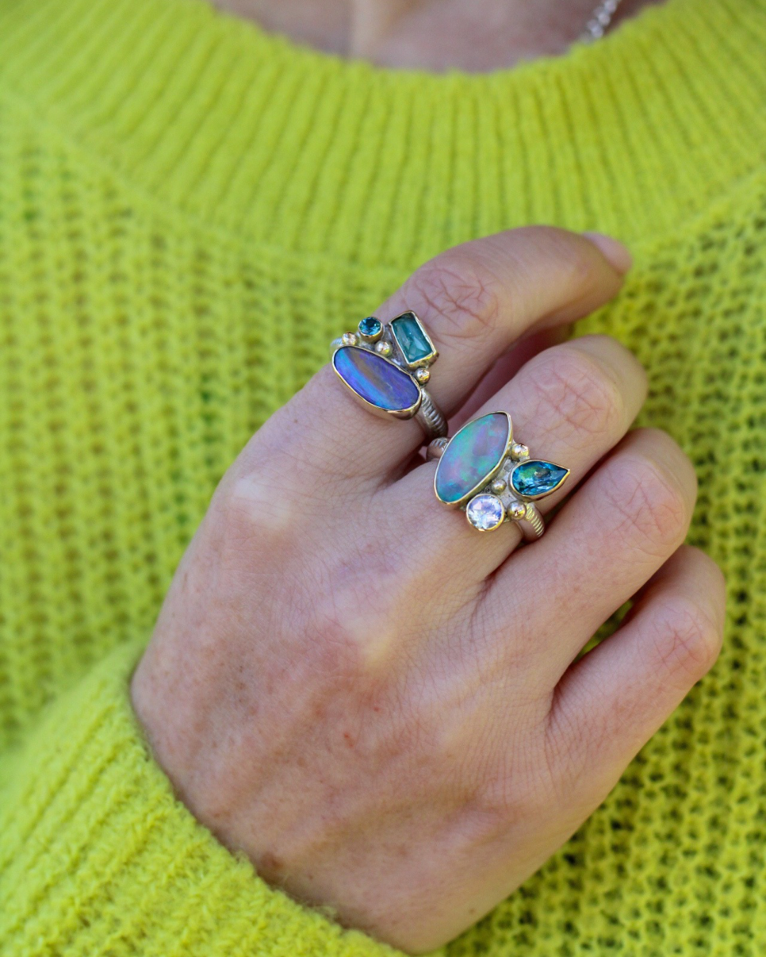 Hand wearing multiple rings with gemstones against a bright green sweater.