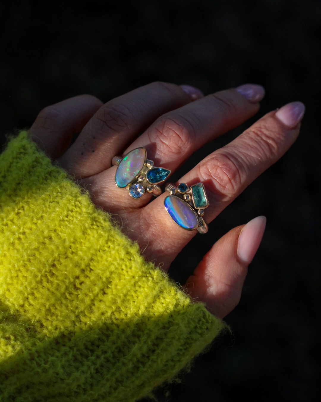 Hand wearing multiple rings with gemstones against a dark background
