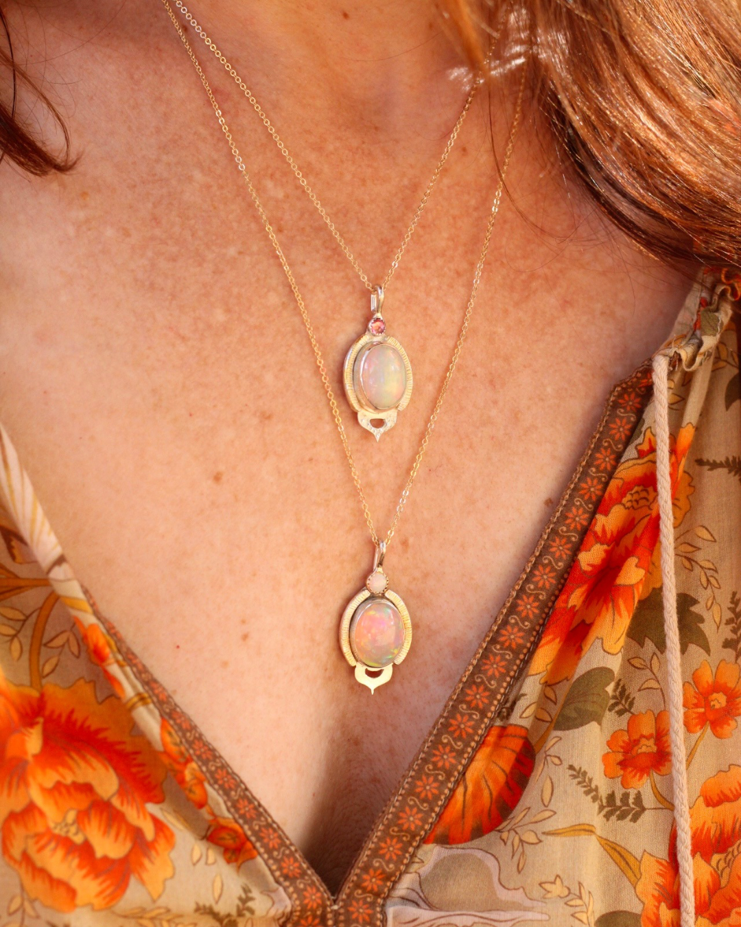 Close-up of a person wearing a gold necklace with opal pendants against a floral garment.