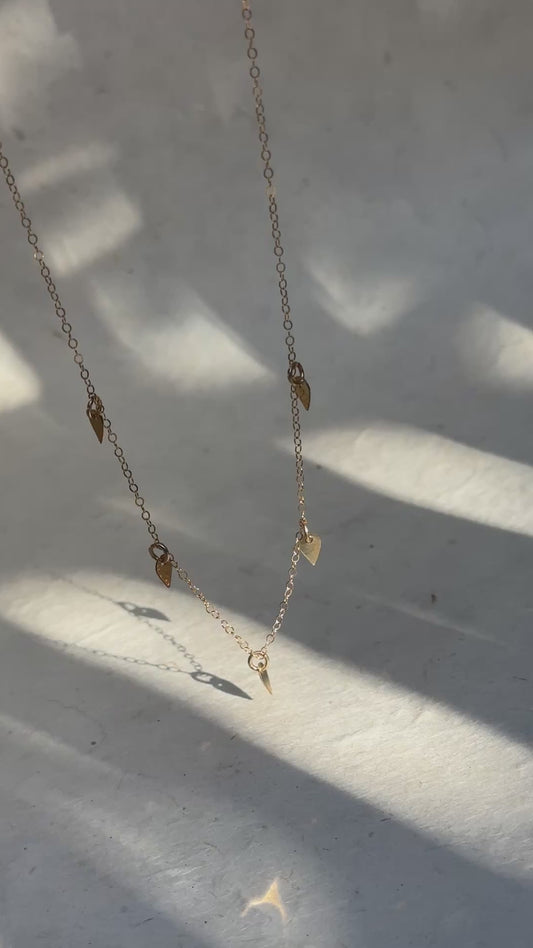a video of a gold dainty necklace with 5 small charms against a white background